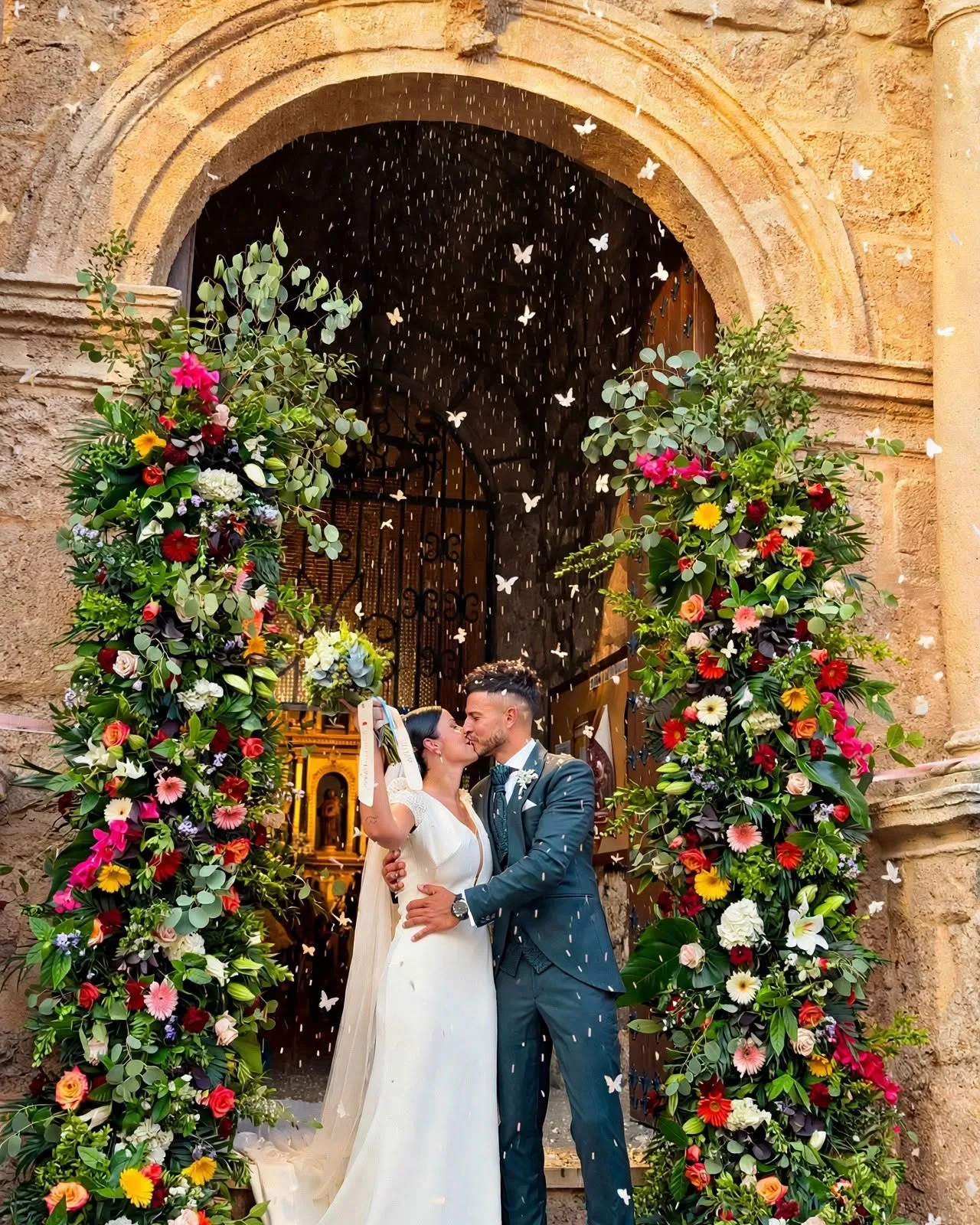 Novios a la salida de la iglesia, con la portada decorada con dos columnas de flores